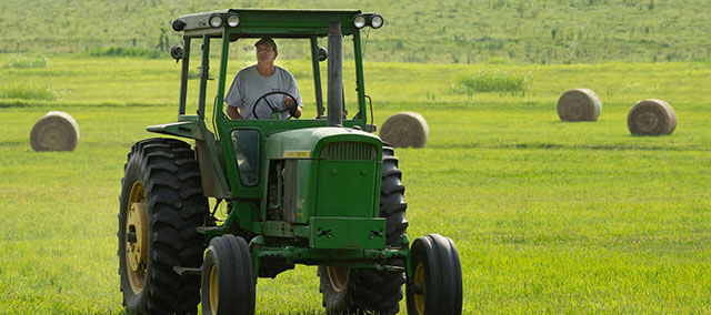 Farmer driving a tractor with haystacks in the background